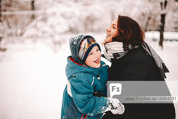 Happy mother embracing playful son in park during winter