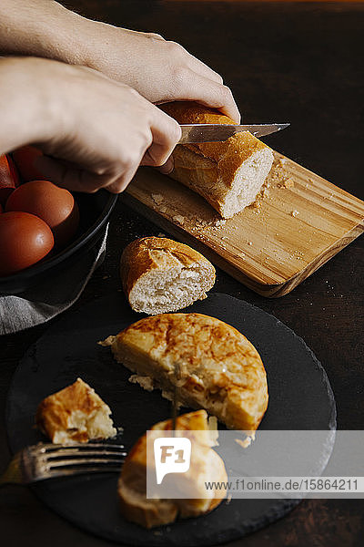 Spanisches Kartoffelomelett  in Scheiben geschnitten und mit Brot serviert. Im Hintergrund schneidet eine Frau einige Brotscheiben.
