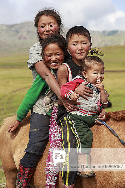 Porträt von vier lächelnden und glücklichen Nomadengeschwistern auf ihrem zahmen Pferd im Sommernomadenlager  Khujirt  Uvurkhangai  Zentralmongolei  Zentralasien  Asien