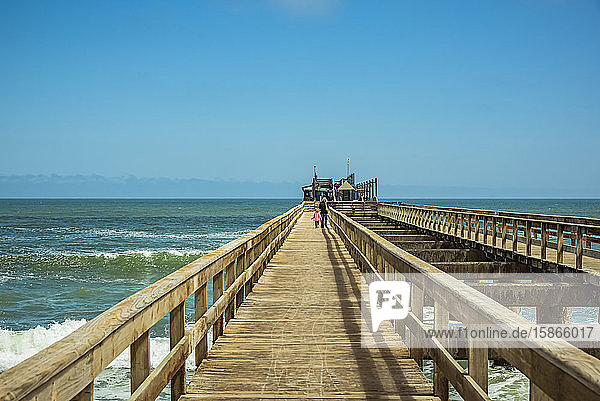 Man and young girl walking on Swakopmund pier Skeleton Coast Dorob National Park; Namibia