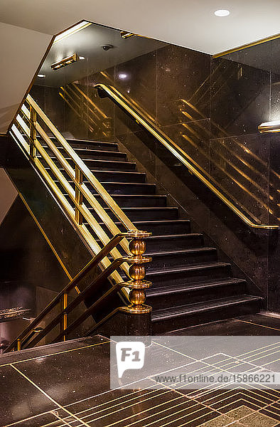 Staircase with brass handrails inside a building with dark brown flooring and walls; New York City New York United States of America