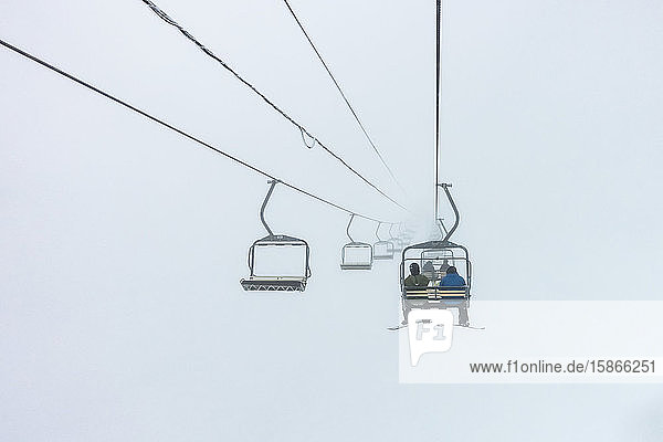 Downhill skiers ride on a chairlift through the clouds Sun Peaks Resort; Sun Peaks British Columbia Canada