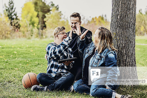 A young man with Down Syndrome celebrates with a high-5 after winning a game on his pad while enjoying quality time with his father and mother in a city park on a warm fall evening: Edmonton  Alberta  Canada