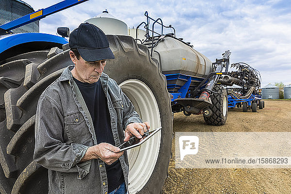 Farmer using a tablet while standing on a farm beside equipment; Alberta  Canada