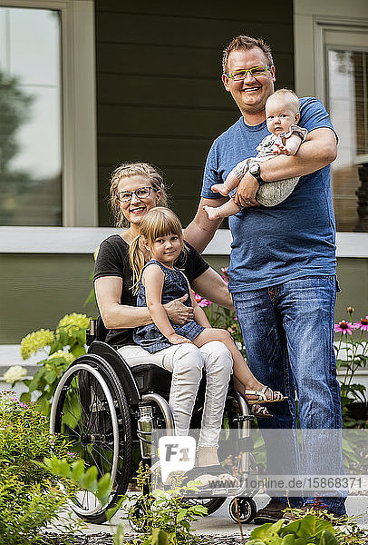 A young family posing for a family portrait outdoors in their front yard and the mother is a paraplegic in a wheelchair; Edmonton  Alberta  Canada