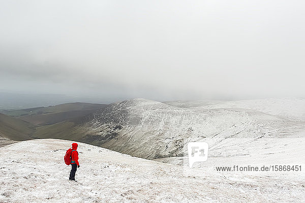 Wanderin in roter Jacke beim Wandern auf einem schneebedeckten Berg im Winter bei schlechtem Wetter  Galty Mountains; County Tipperary  Irland