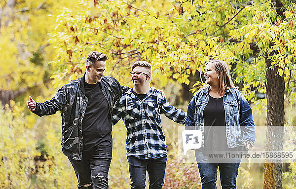 A young man with Down Syndrome walking with his father and mother while enjoying each other's company in a city park on a warm fall evening: Edmonton  Alberta  Canada