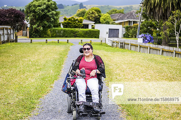 Maori-Frau mit Cerebralparese in einem Rollstuhl  die einen Bürgersteig entlangfährt; Wellington  Neuseeland