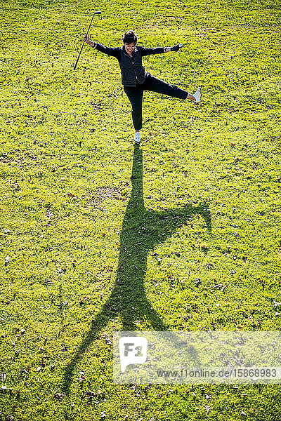 Hohe Winkelansicht einer Golferin auf grünem Gras  die ihren Schläger und Ball in die Luft hält und einen Schatten auf den Boden wirft; Schweiz