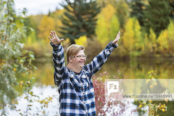 Ein junger Mann mit Down-Syndrom hebt an einem warmen Herbstabend in einem Stadtpark seine Hände zur Anbetung Gottes: Edmonton  Alberta  Kanada