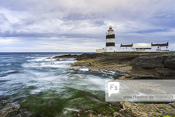 Hook Head lighthouse  Black and white lighthouse on rocky shore on a cloudy summer day.  long exposure; County Waterford  Ireland