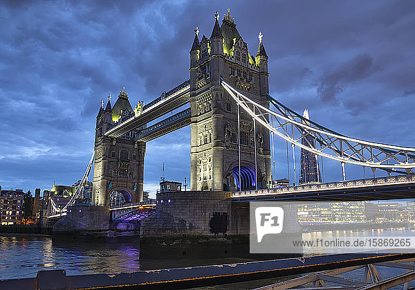 Tower Bridge beleuchtet in der Abenddämmerung und reflektiert im ruhigen Wasser der Themse; London  England