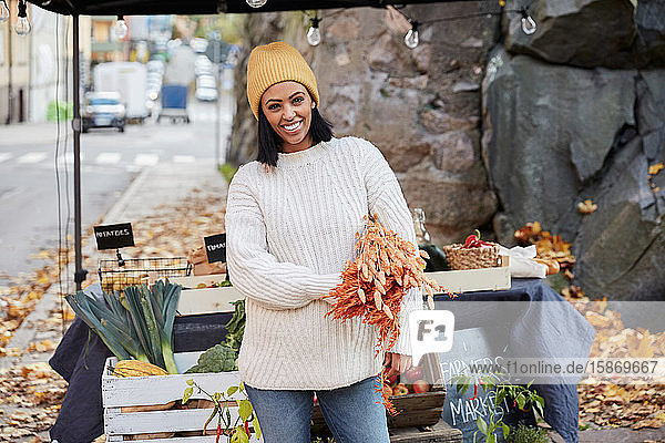 Portrait of happy woman standing with crops at market stall