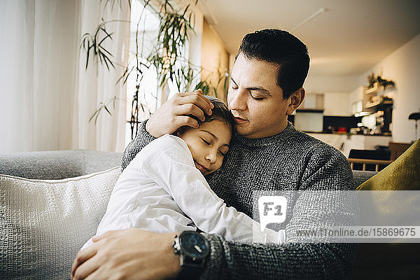 Girl sleeping while hugging father on sofa at home