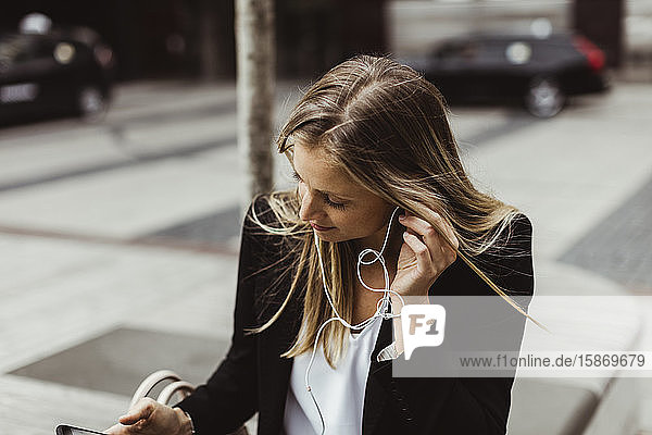 Geschäftsfrau mit In-Ear-Kopfhörern im Freien sitzend