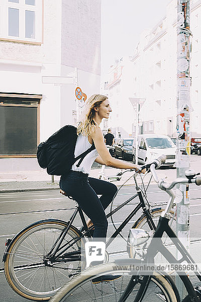 Side view of young woman riding bicycle on street in city