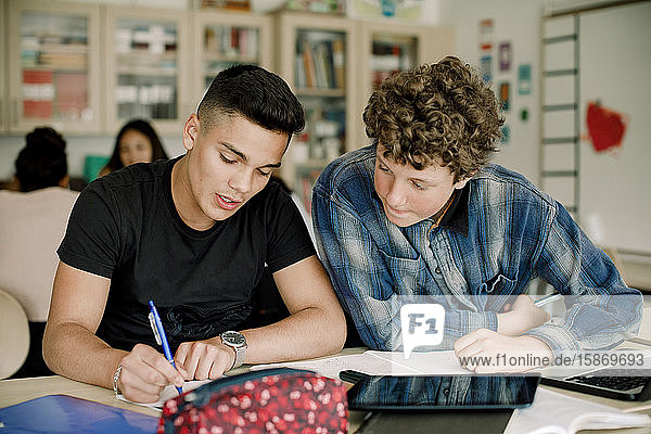 Männliche Studenten lernen am Tisch  während sie im Klassenzimmer sitzen