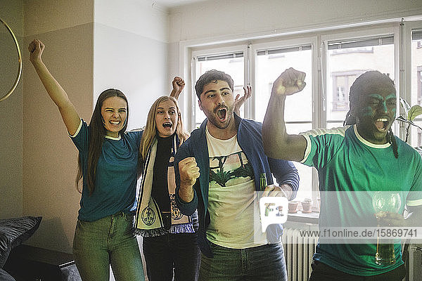 Junge fröhliche Freunde sehen sich ein Fußballspiel an  während sie im Wohnzimmer stehen
