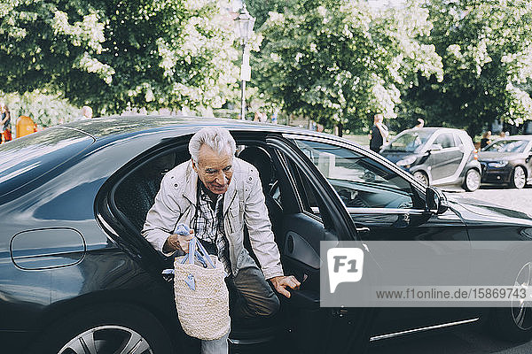 Älterer Mann hält Tasche und steigt aus schwarzem Auto in der Stadt aus