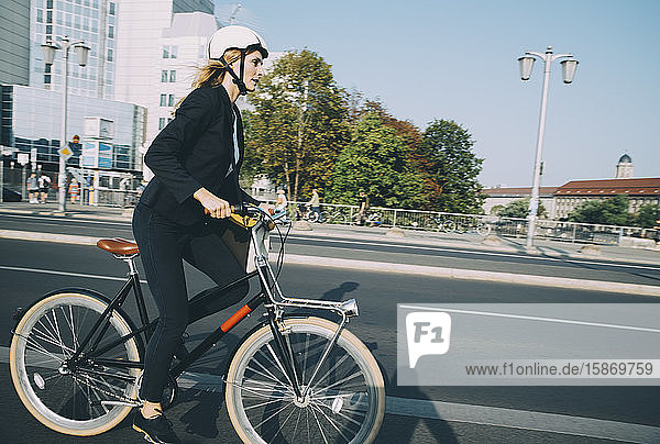 Side view of businesswoman riding bicycle on city street against sky
