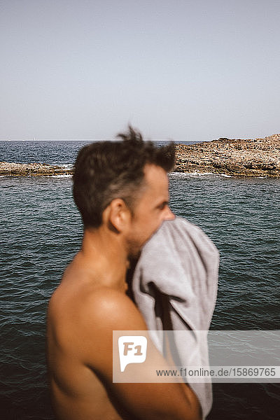 Seitenansicht eines Mannes beim Trocknen des Gesichts mit einem Handtuch am Meer an einem sonnigen Tag