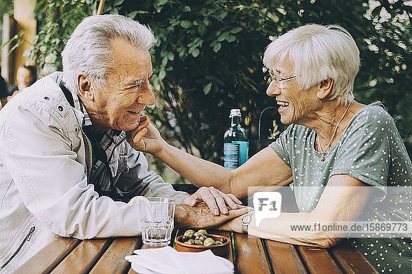 Lächelnde ältere Frau berührt die Wange ihres Partners  während sie in einem Restaurant in der Stadt sitzt