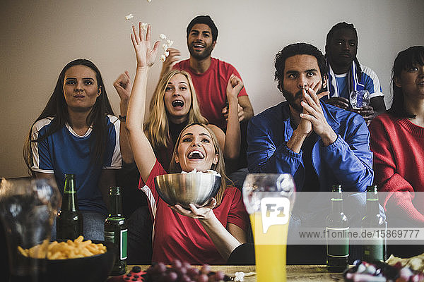 Männliche und weibliche Fußballfans sehen sich das Spiel an  während sie zu Hause auf dem Sofa sitzen