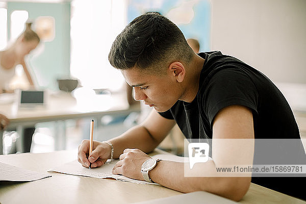 Teenage boy studying while sitting by table in classroom