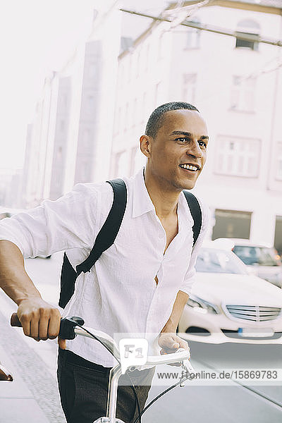 Lächelnder Geschäftsmann mit Fahrrad auf dem Bürgersteig in der Stadt
