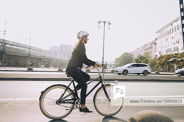 Eine weibliche Führungskraft in voller Länge mit Helm fährt Fahrrad auf der Straße in der Stadt