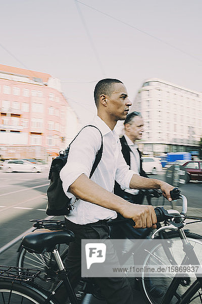 Männliche Unternehmer fahren Fahrrad auf Straße in Stadt gegen Himmel