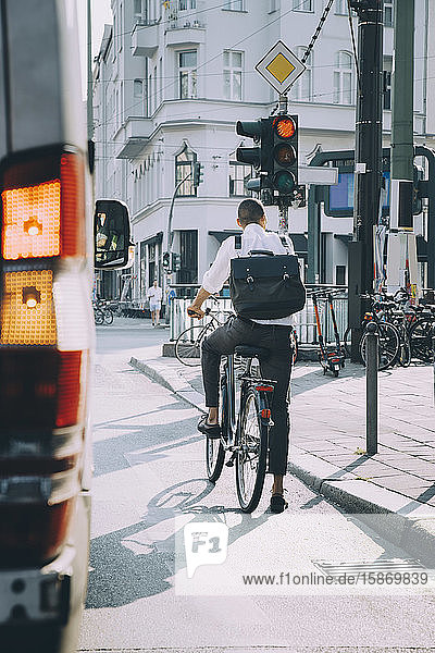 Rückansicht eines männlichen Unternehmers auf dem Fahrrad auf der Straße in der Stadt