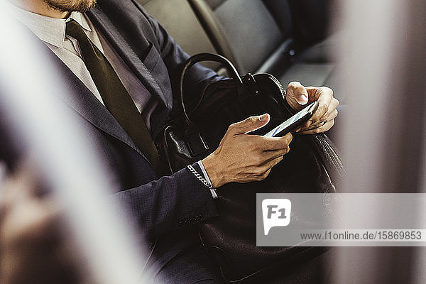 Mittelteil eines Geschäftsmannes  der ein Smartphone benutzt  während er im Auto sitzt