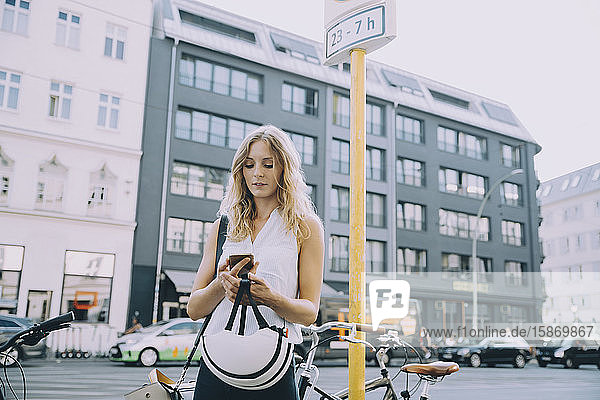Junge Geschäftsfrau benutzt Mobiltelefon  während sie in der Stadt auf der Straße steht