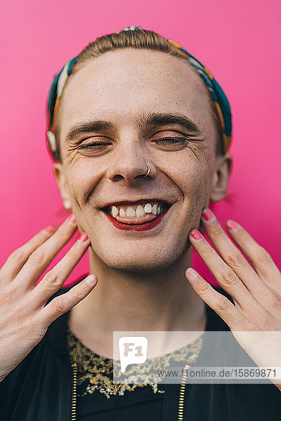 Porträt eines glücklichen jungen Mannes mit Zunge  der vor rosa Hintergrund steht