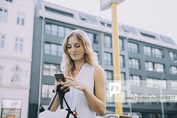 Lächelnde Geschäftsfrau mit Smartphone gegen Gebäude in der Stadt