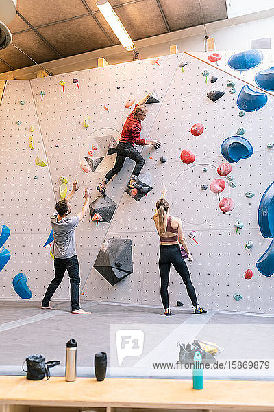 Mature coach showing wall climbing to male and female in gym