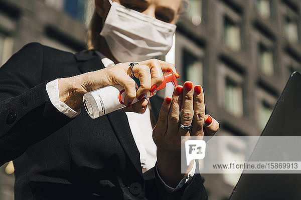 Geschäftsfrau mit Gesichtsmaske mit Handdesinfektionsmittel