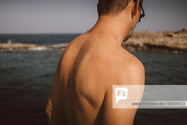 Rückansicht eines hemdlosen Mannes am Strand an einem sonnigen Tag