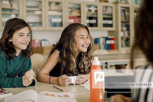 Smiling female student with paper sitting by friend in classroom