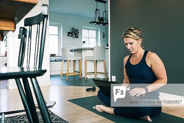 Frau arbeitet über Laptop  während sie zu Hause auf einer Matte im Wohnzimmer sitzt