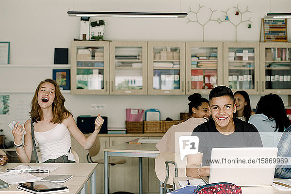 Portrait of male students using laptop while smiling female teenagers sitting in classroom