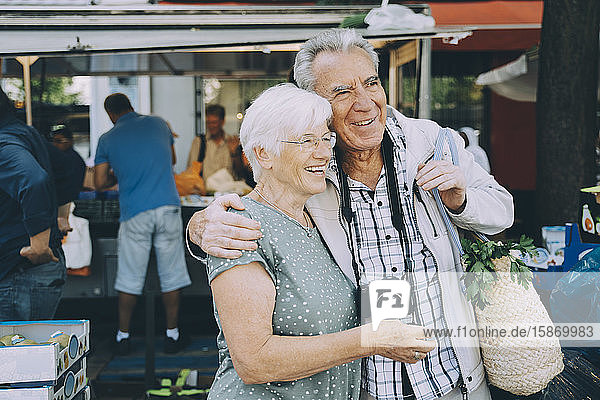 Lächelndes älteres Ehepaar mit Arm um den Arm auf dem Markt in der Stadt stehend
