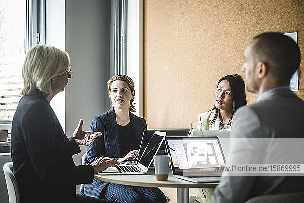 Leitende Geschäftsfrau bespricht Strategien mit Kollegen  während sie im Sitzungssaal sitzt
