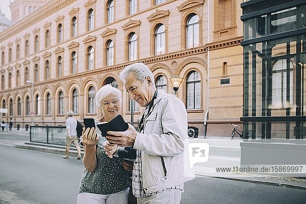 Smiling senior male and female tourist using smart phone while exploring in city
