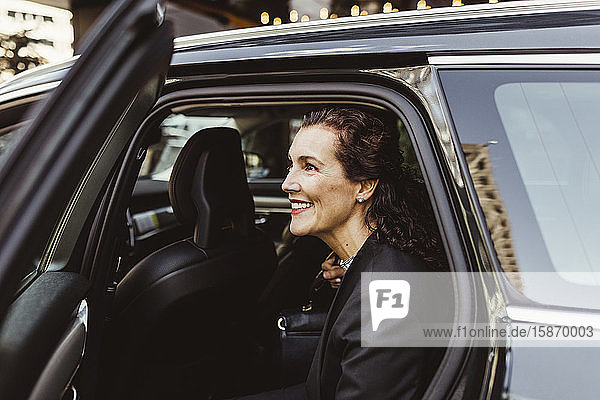 Lächelnde Unternehmerin schaut beim Aussteigen aus dem Auto weg