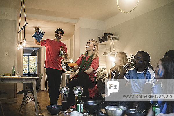 Smiling male and female friends watching soccer match in living room