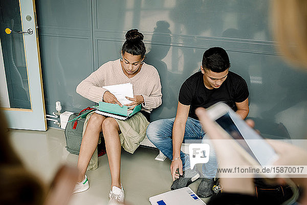 Männliche und weibliche Schüler erledigen Hausaufgaben  während sie auf dem Schulflur sitzen