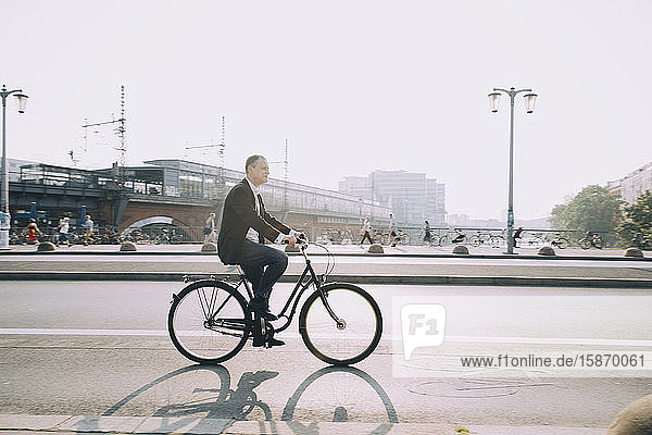 Side view of male entrepreneur riding bicycle on city street against sky