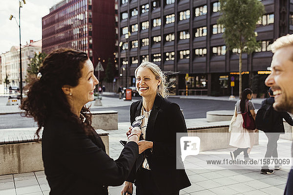 Unternehmerin lächelt mit ihren Mitarbeitern  während sie im Freien steht